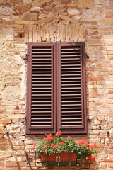 Fototapeta na wymiar Typical house facade with red geraniums in San Gimignano, Tuscany Italy