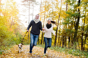 Fototapeta premium Beautiful young couple with dog running in autumn forest