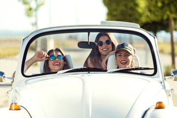 Three pretty young women driving on road trip on beautiful summe