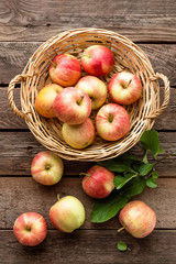 Fresh red apples in wicker basket on wooden table.