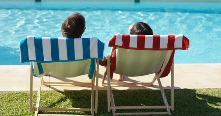 Couple relaxing in colorful deck chairs at the pool enjoying the hot summer sun  view from the rear...