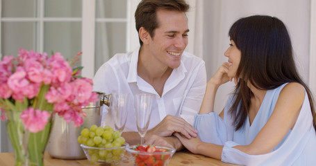 Cute mixed couple enjoying wine and fruit snacks together at table with pink flower bouquet