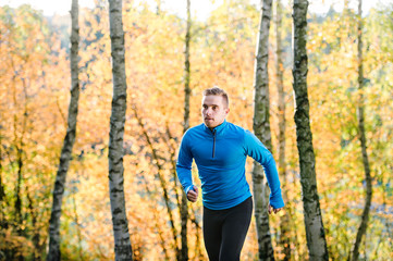 Young handsome athlete running outside in sunny autumn nature