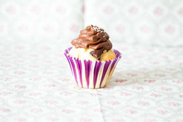 Vanilla-chocolate cupcake with topping on a light floral background.