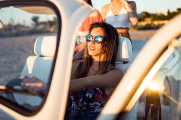 Three pretty young women driving on road trip on beautiful summe
