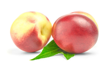 two ripe nectarines with green leaves over white background