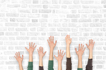 Many hands up on the background of a brick wall