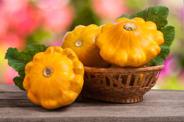 yellow pattypan squash with leaf in a wicker basket on  wooden table   blurred background