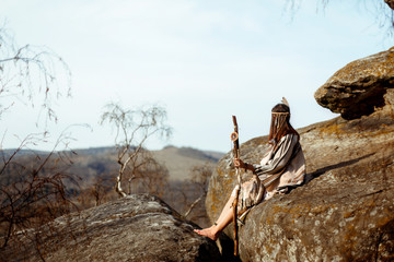 beautiful boho woman holding pikestaff sitting on rocks