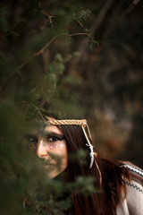 beautiful boho  woman with warrior shaman makeup hiding in tree
