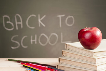 School books and apple against blackboard