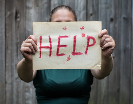 A girl holding a sheet of paper on which is written "help".
