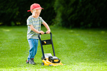 Cute boy mows lawn by yellow lawn mower