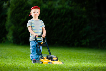 Cute boy mows lawn by yellow lawn mower