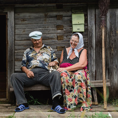 beautiful mature russian couple have fun outside of their house in village. The woman clothed in a scarf keeps the broom. They stroking domestic cat.