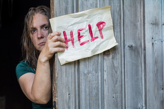 A girl stands in front of the open door, and holding a piece of paper with the word "help"

