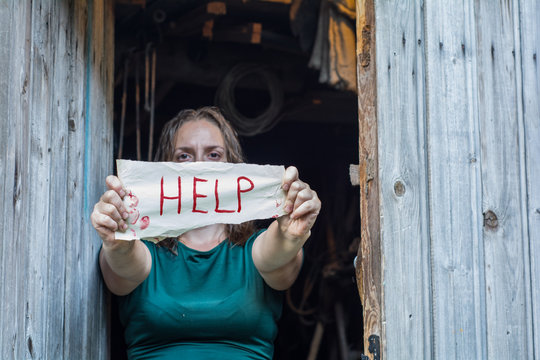 A girl stands in front of the open door, and holding a piece of paper with the word "help"
