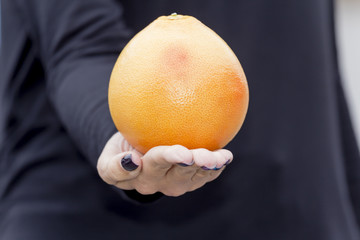 On the Palm of the hand of the girl is a big orange grapefruit.