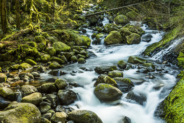 Stream leading to triple falls on hike in Oregon by Columbia River Gorge with mossy rocks and soft smooth flowing water