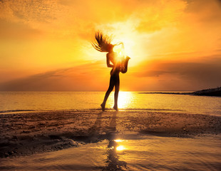 Sexy woman playing saxophone on the beach at sunset