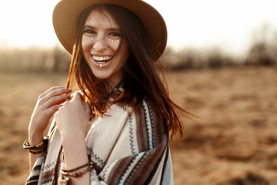 beautiful boho woman hipster, smiling, wearing hat and poncho at sunset in mountains, true emotions, space for text