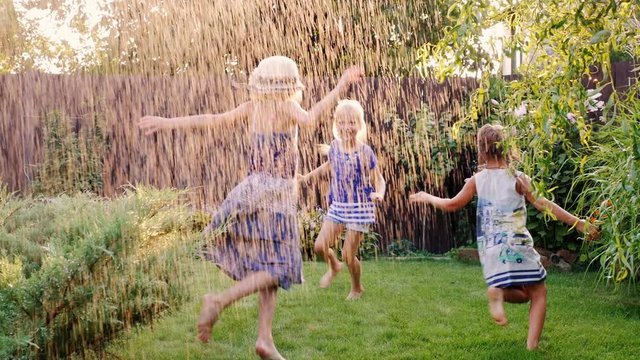 Group of carefree cheerful children playing in the garden. Running around barefoot on the grass under the jets of water or rain.