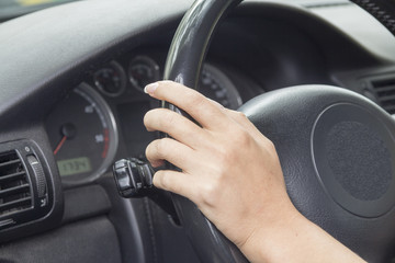 The hand of a girl holding a steering wheel in the car. 