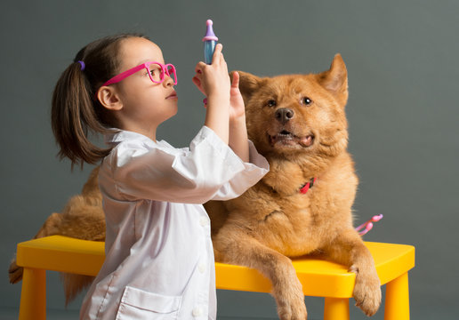 Girl holding a toy syringe and playing veterinarian with dog