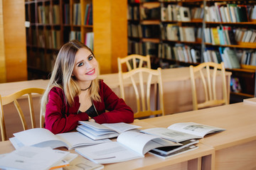 Smiling attractive female student sitting at desk in old university library preparing for exam and reading books. Education process.