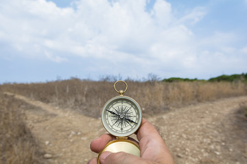 Man holding a compass on a fork in the road on a decision, dilemma, direction concept