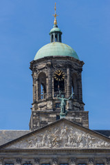 Fototapeta na wymiar Amsterdam, the Netherlands - August 16, 2016: The top of the Royal Palace on the Dam against blue sky. Cut off at triangle mural. Statue, niche and clock.