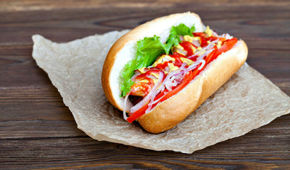 Big tasty hot dog with sauce and vegetables in parchment on the wooden background. hotdog gourmet.