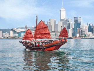 Naklejka premium Hong Kong traditional red-sail Junk boat on city skyscrapers background
