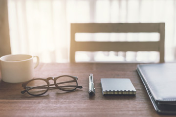 Notebook and cup of coffee with sunlight on desk office