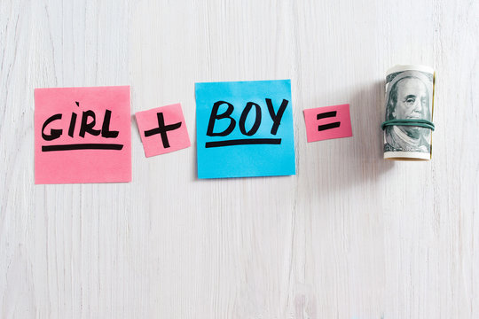 Girl plus boy equals money composition, copy space. Top view on pink and blue stickers with text and pack of money on white wooden background, free space. Concept of expence having a baby
