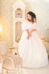 Fototapeta premium Pretty adult woman wearing vintage beautiful white dress standing in bright retro room