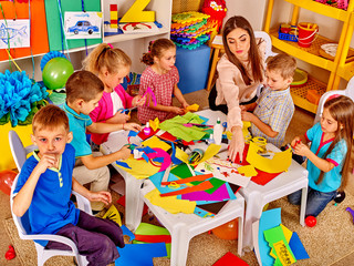 Large group of children with teacher are making something out of colored paper on table in primary school. Childrens crafts out of paper. Top view of primary school.