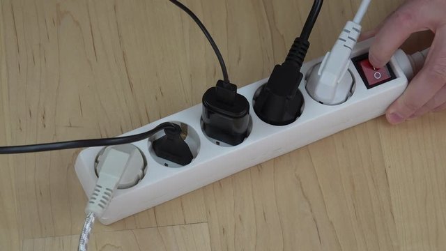 man hands insert wire plugs and turn on extension switch on wooden floor.