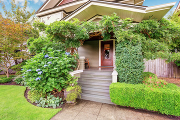 Cozy covered porch sinking in green bushes and trees.