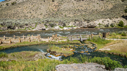 Fototapeta na wymiar Wooden bridge across the river on a background of mountains. Rocky shore of the river. Amazing landscape of riverside. River in the mountains. Boiling River Trail, Yellowstone National Park, Wyoming 