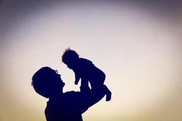 silhouettes of father and little baby playing at sunset