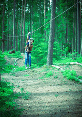 Toned image brave little boy in helmet and harness zip lining at adventure park on the background of pine trees