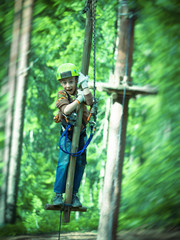 Toned image brave little boy in helmet and harness zip lining at adventure park on the background of pine trees