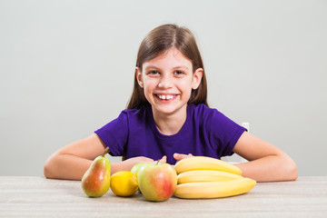 Fototapeta premium Happy little girl is sitting with fruit at table.