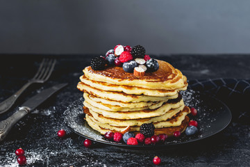 Stack of pancakes with fresh fruits, nuts and powdered sugar on dark background