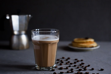 Latte coffee in a high glass, moka coffee maker, a plate of pancakes on a dark gray concrete background, horizontal photo