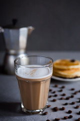 Latte coffee in a high glass, moka coffee maker, a plate of pancakes on a dark gray concrete background, vertical photo