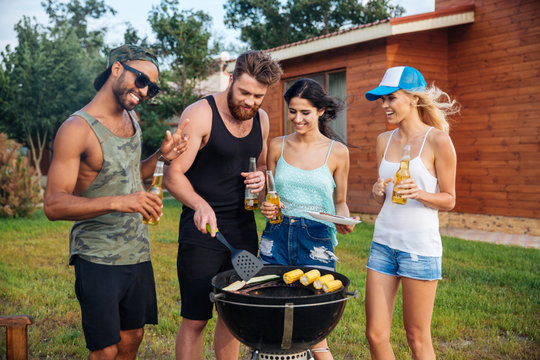 Smiling people drinking beer and cooking on barbeque grill outdoors