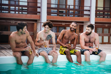 Group of men sitting and drinking beer near swimming pool
