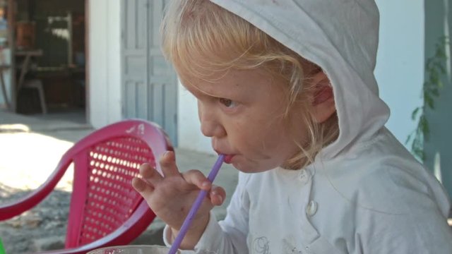 Little Girl Sits at Table Drinks Juice in Sideroad Cafe Closeup